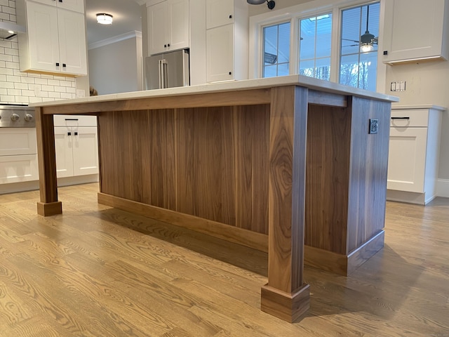 kitchen featuring appliances with stainless steel finishes, white cabinetry, backsplash, ornamental molding, and light hardwood / wood-style floors