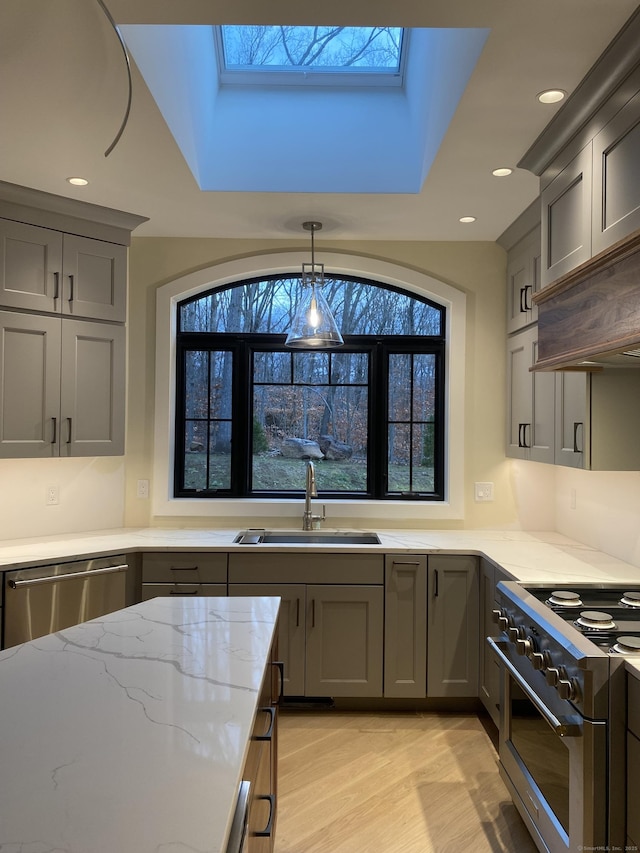 kitchen featuring sink, light stone counters, decorative light fixtures, a skylight, and appliances with stainless steel finishes