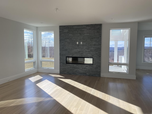 unfurnished living room with plenty of natural light, a stone fireplace, and dark hardwood / wood-style flooring