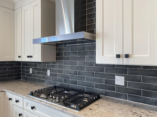 kitchen with tasteful backsplash, white cabinetry, stainless steel gas stovetop, light stone counters, and wall chimney range hood