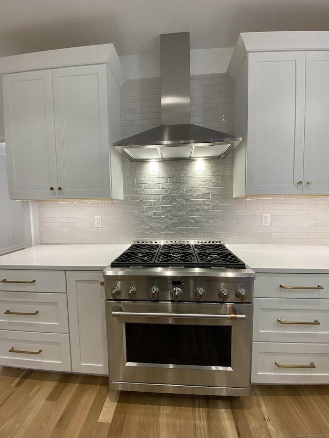 kitchen with high end stainless steel range oven, white cabinets, and wall chimney range hood