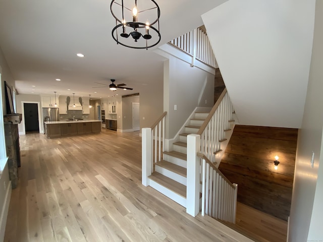 staircase with hardwood / wood-style flooring, sink, and ceiling fan with notable chandelier