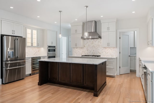 kitchen with wall chimney range hood, stainless steel appliances, a center island, white cabinets, and beverage cooler