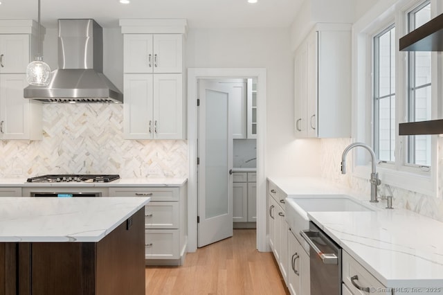 kitchen featuring appliances with stainless steel finishes, decorative light fixtures, white cabinetry, sink, and wall chimney range hood