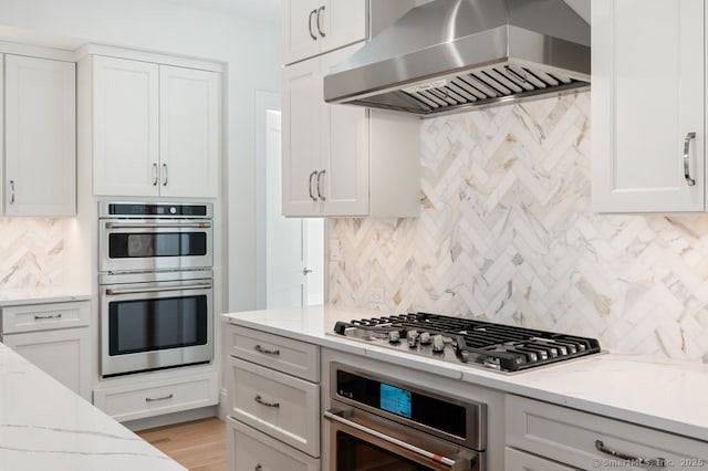 kitchen with range hood, stainless steel appliances, tasteful backsplash, light stone countertops, and white cabinets