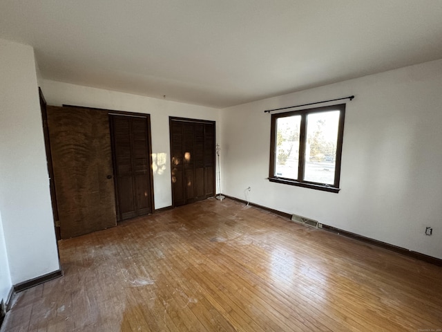 unfurnished bedroom featuring hardwood / wood-style flooring and multiple closets