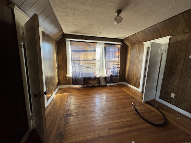 interior space featuring wood-type flooring, vaulted ceiling, radiator, and wooden walls