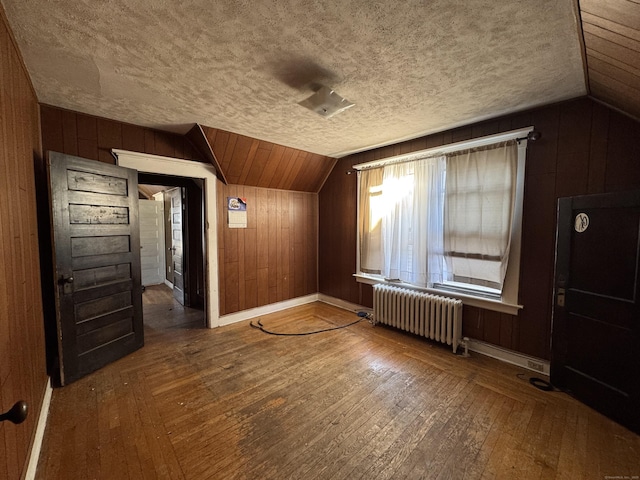 additional living space with hardwood / wood-style flooring, wooden walls, radiator, and vaulted ceiling