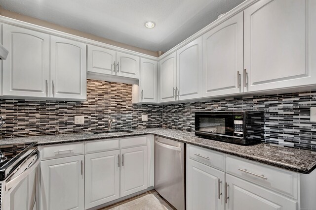 kitchen with appliances with stainless steel finishes, dark stone countertops, white cabinetry, and sink