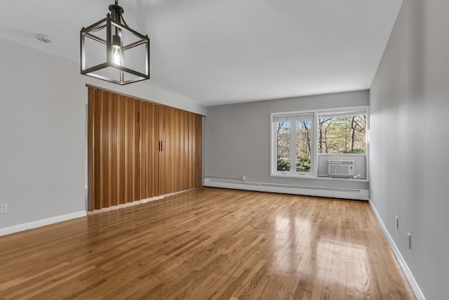 unfurnished living room with baseboard heating, a wall mounted AC, wood-type flooring, and a notable chandelier