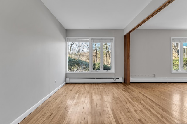 spare room with a baseboard radiator, a wealth of natural light, and light wood-type flooring