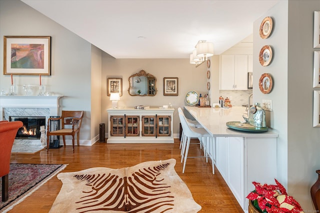 kitchen featuring kitchen peninsula, hanging light fixtures, a high end fireplace, hardwood / wood-style flooring, and white cabinetry