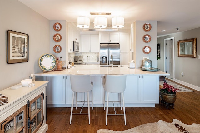 kitchen with white cabinets, kitchen peninsula, appliances with stainless steel finishes, and pendant lighting