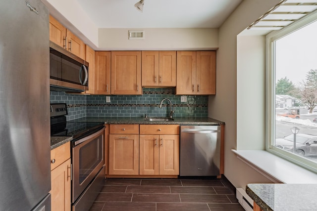 kitchen featuring sink, dark stone countertops, a baseboard heating unit, stainless steel appliances, and tasteful backsplash