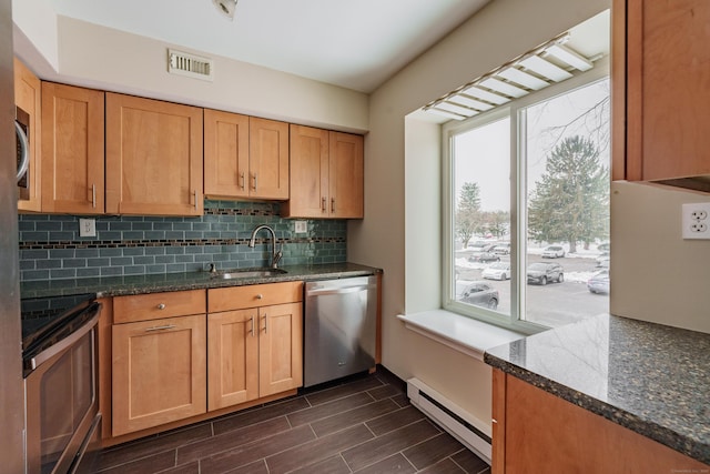 kitchen featuring sink, dark stone counters, a baseboard radiator, stainless steel appliances, and decorative backsplash