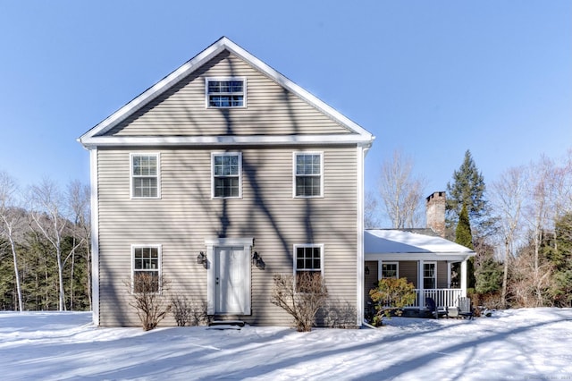 snow covered back of property featuring covered porch