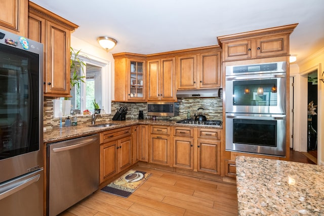 kitchen featuring light stone countertops, light hardwood / wood-style floors, decorative backsplash, appliances with stainless steel finishes, and ornamental molding