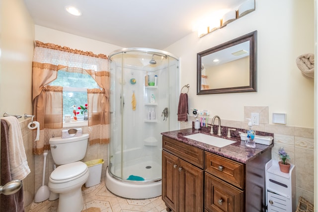 bathroom featuring tile patterned flooring, toilet, vanity, tile walls, and a shower with shower door