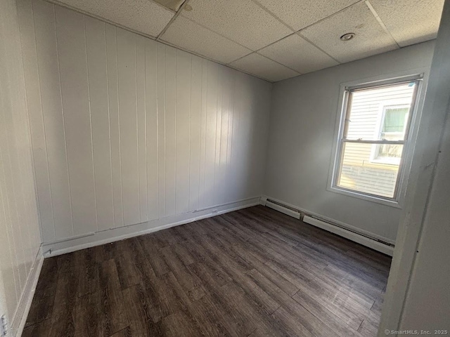 empty room with baseboard heating, a drop ceiling, and dark hardwood / wood-style flooring