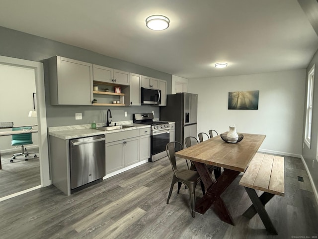 kitchen featuring stainless steel appliances, a sink, dark wood-type flooring, light countertops, and baseboards