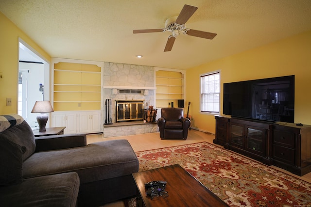 living room with ceiling fan, a stone fireplace, built in features, and a textured ceiling