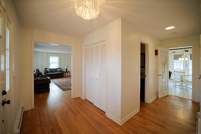 hall featuring hardwood / wood-style floors, a notable chandelier, baseboard heating, and french doors