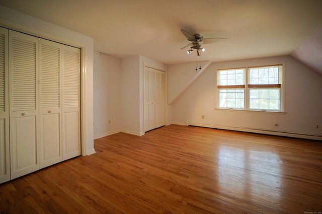 unfurnished bedroom with lofted ceiling, a baseboard heating unit, light hardwood / wood-style flooring, ceiling fan, and multiple closets