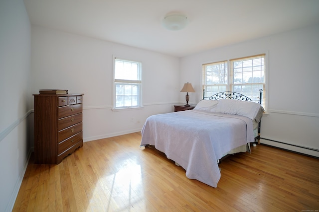 bedroom with light wood-type flooring, a baseboard radiator, and multiple windows