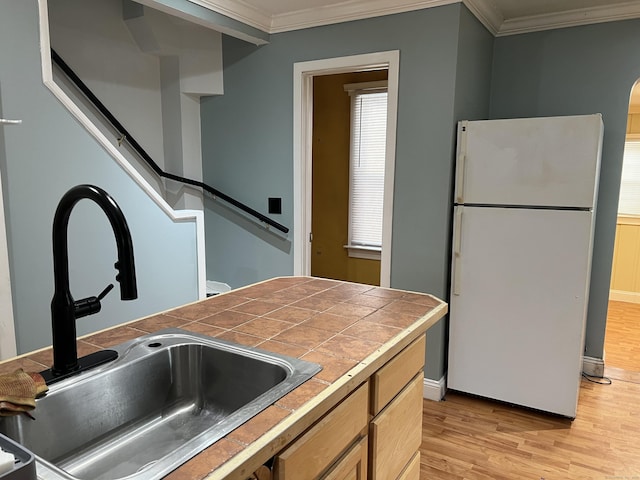 kitchen with sink, white refrigerator, tile counters, light hardwood / wood-style floors, and crown molding