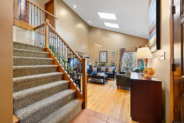 stairs with high vaulted ceiling, a skylight, and tile patterned flooring