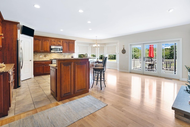 kitchen featuring stainless steel appliances, a chandelier, pendant lighting, decorative backsplash, and a kitchen island