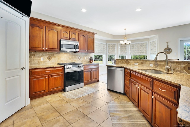 kitchen with sink, hanging light fixtures, stainless steel appliances, light stone counters, and a notable chandelier