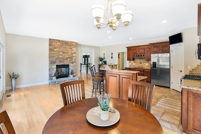 dining room with a stone fireplace, light wood-type flooring, and an inviting chandelier