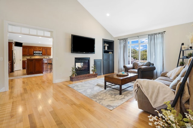 living room with high vaulted ceiling, a brick fireplace, and light hardwood / wood-style flooring