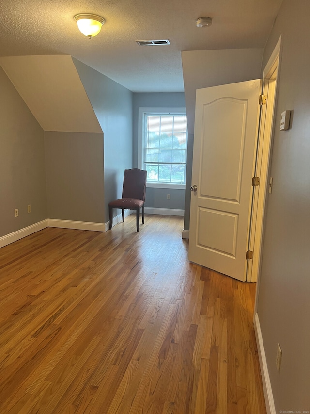 additional living space with vaulted ceiling, a textured ceiling, and light wood-type flooring