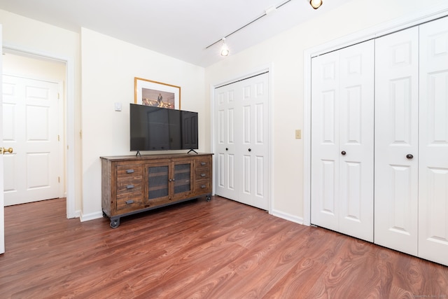 bedroom with multiple closets, rail lighting, and hardwood / wood-style flooring