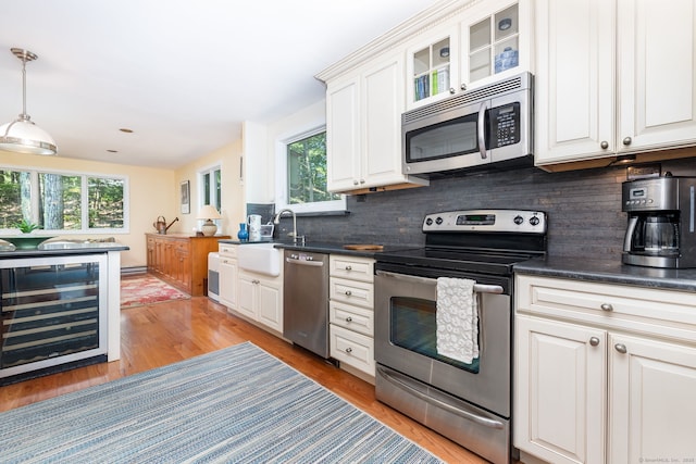 kitchen featuring appliances with stainless steel finishes, wine cooler, sink, white cabinetry, and hanging light fixtures