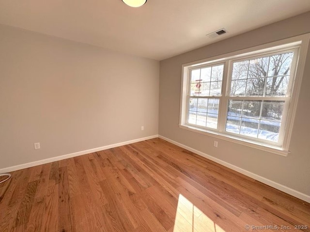 empty room with light wood-type flooring, visible vents, and baseboards