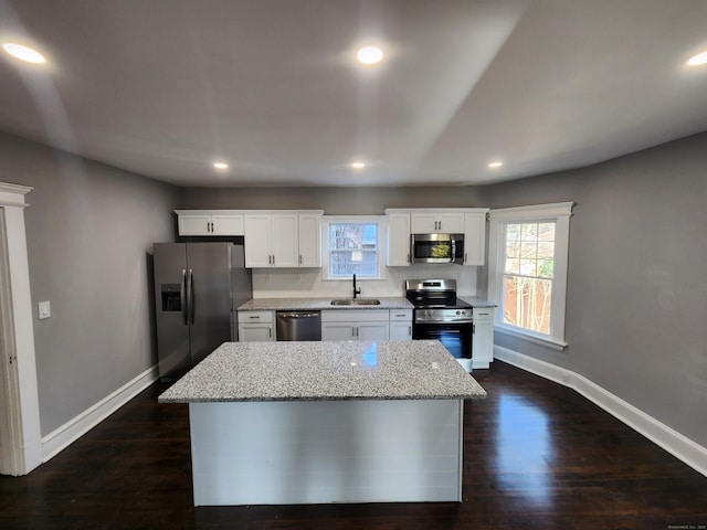 kitchen with a center island, sink, light stone countertops, appliances with stainless steel finishes, and white cabinetry