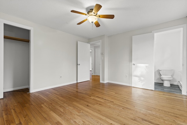 unfurnished bedroom with light hardwood / wood-style floors, ceiling fan, connected bathroom, a baseboard radiator, and a closet