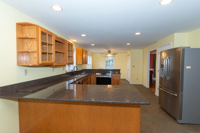 kitchen with ceiling fan, kitchen peninsula, sink, appliances with stainless steel finishes, and dark stone counters