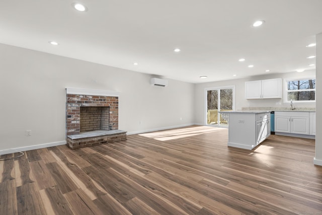 kitchen with a wall mounted AC, dark hardwood / wood-style flooring, a brick fireplace, white cabinets, and sink