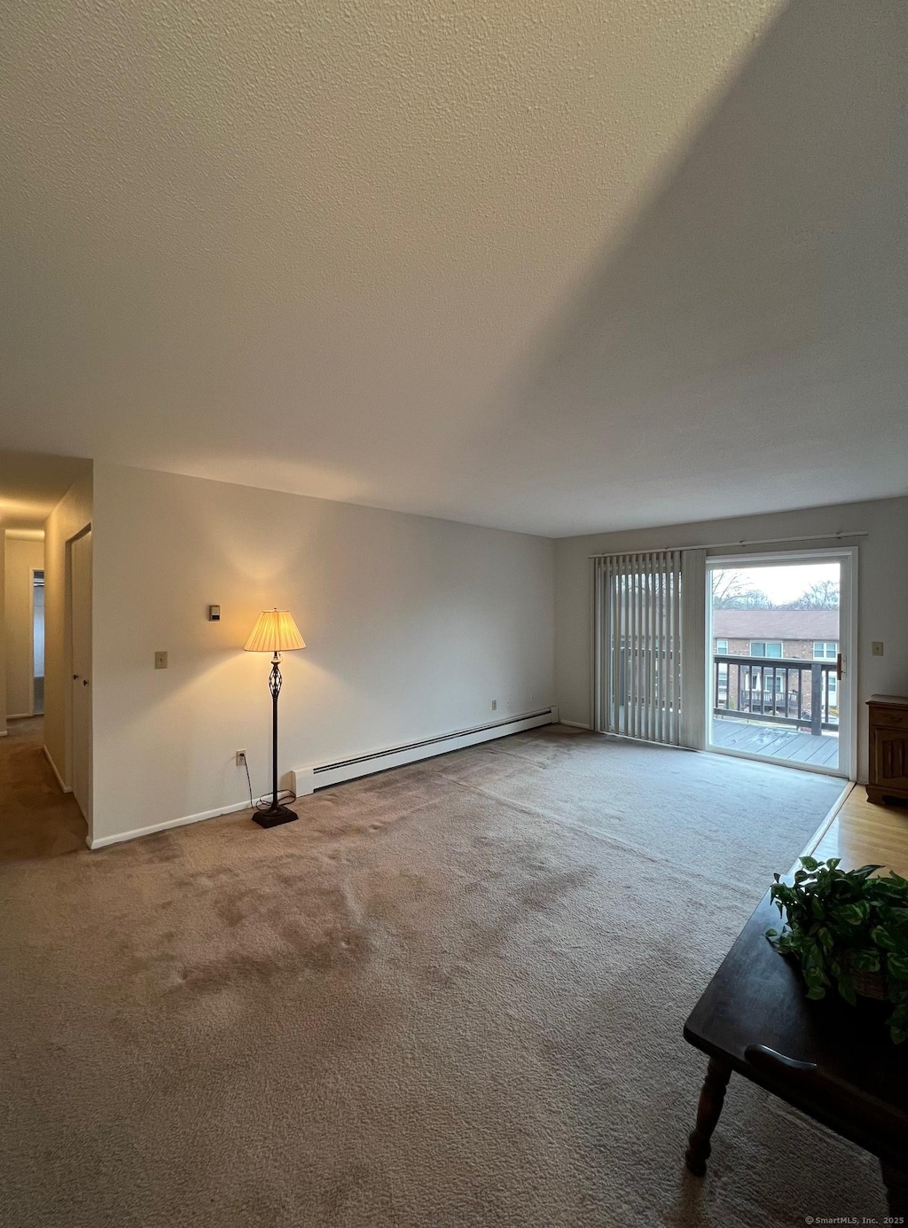 unfurnished living room with carpet floors, a textured ceiling, and baseboard heating