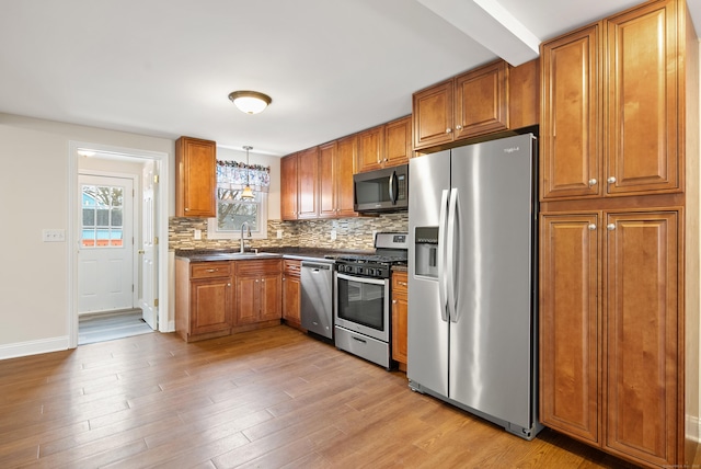 kitchen with tasteful backsplash, stainless steel appliances, sink, decorative light fixtures, and light hardwood / wood-style flooring