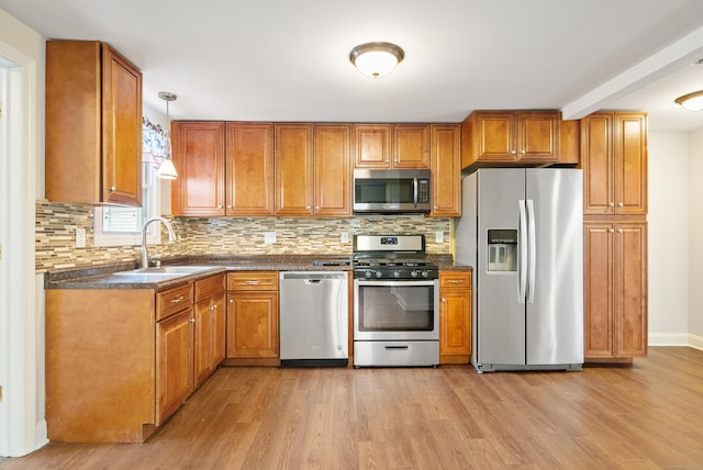 kitchen with backsplash, sink, hanging light fixtures, light hardwood / wood-style floors, and stainless steel appliances