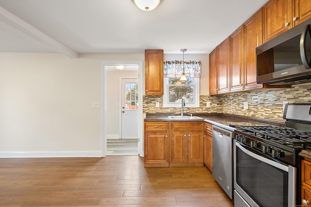 kitchen featuring pendant lighting, sink, light wood-type flooring, tasteful backsplash, and stainless steel appliances