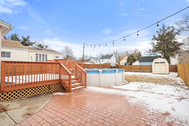 snow covered patio featuring a swimming pool side deck and a storage shed