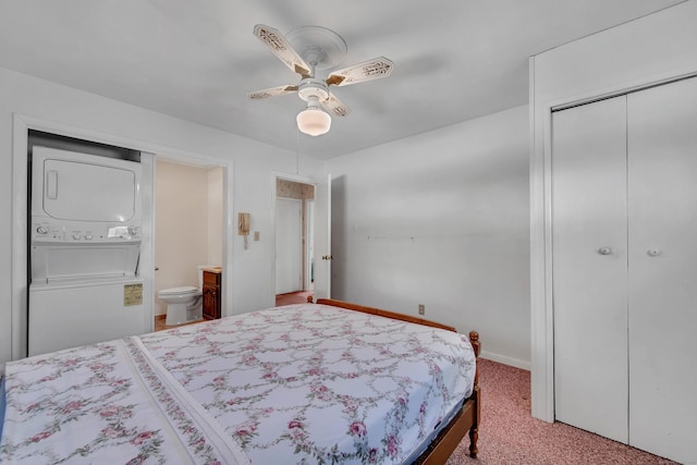 bedroom with ensuite bathroom, stacked washer and dryer, a closet, carpet, and ceiling fan