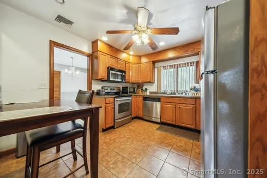 kitchen with light tile patterned floors, ceiling fan with notable chandelier, and stainless steel appliances