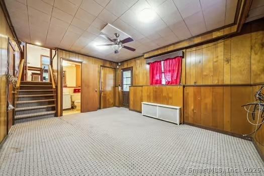 basement with carpet, ceiling fan, and wood walls